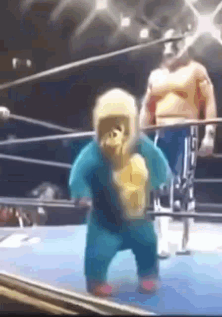 a baby monkey is walking in a boxing ring while a man stands behind him .