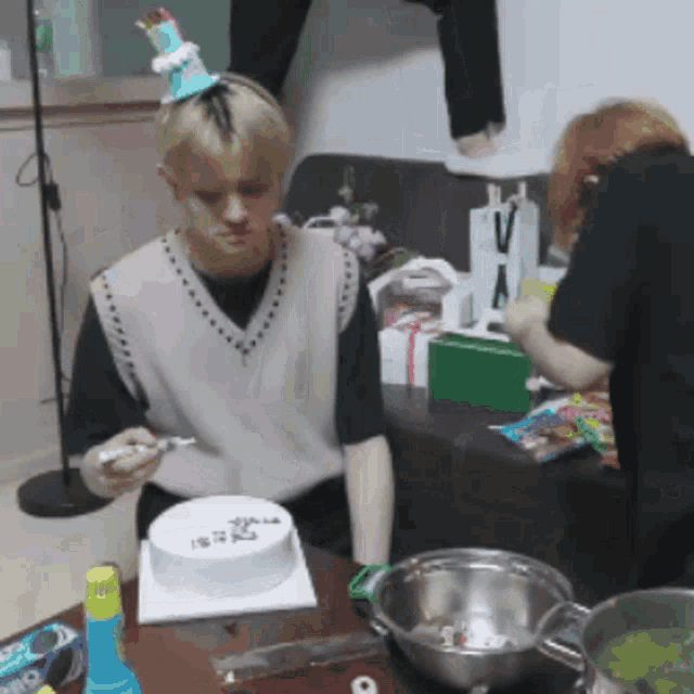 a man wearing a party hat sits at a table with a birthday cake