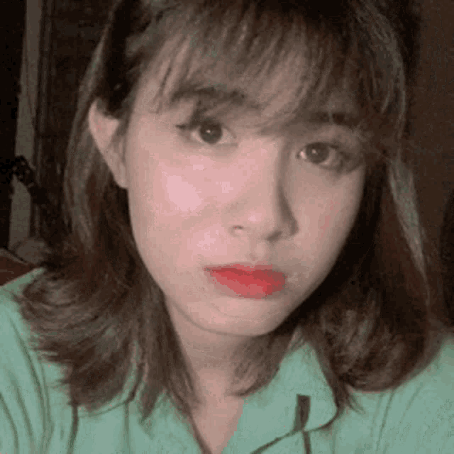 the woman is wearing a green shirt and red lipstick .