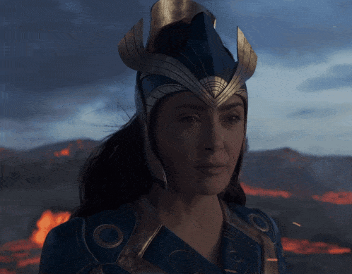 a woman wearing a blue and gold helmet stands in front of a burning mountain