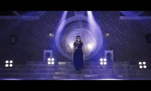 a woman in a blue dress stands on a stage in front of a mirror