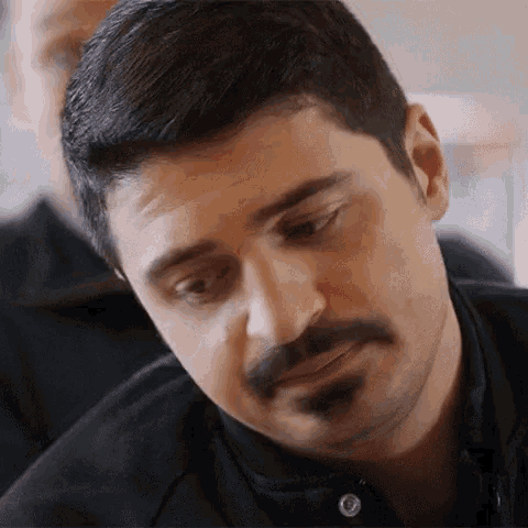 a man with a mustache and beard is looking down at something .