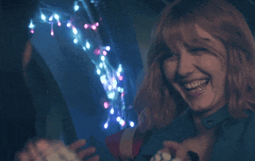 a woman in a blue jacket is smiling in front of a christmas tree