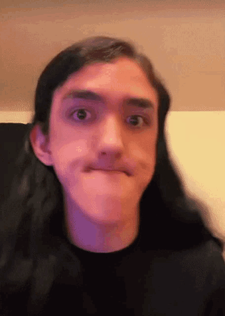 a young man with long hair is making a funny face while wearing a black shirt .