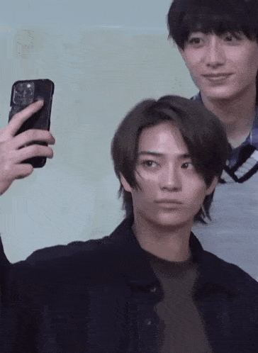 a young man is taking a selfie with his phone while another young man looks on .