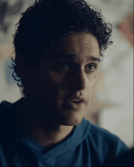 a close up of a man 's face with curly hair wearing a blue shirt