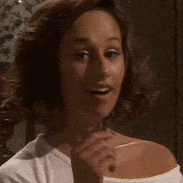 a woman is smoking a cigarette in a dark room while wearing a white shirt .