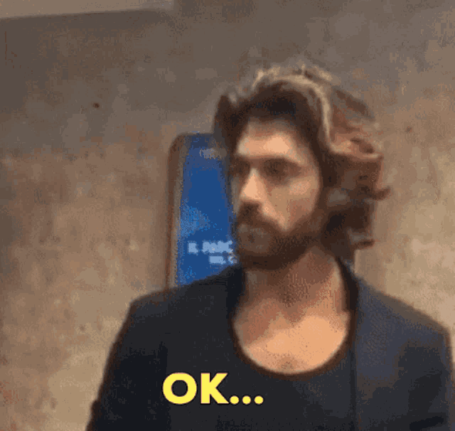 a man with long hair and a beard is saying " ok "