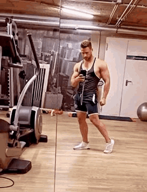 a man is taking a selfie in a gym while looking at his phone .