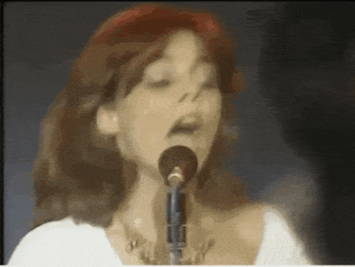 a woman singing into a microphone with a red headband
