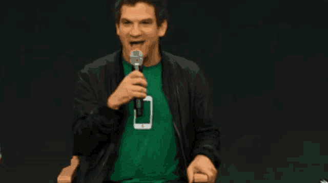 a man wearing a green shirt with an iphone on it holds a microphone