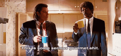 two men in suits and ties are standing in a kitchen drinking coffee and talking .