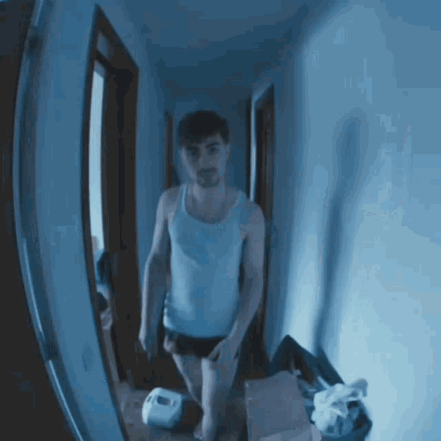a man in a tank top is standing in a dark hallway