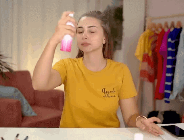 a woman wearing a yellow shirt that says good vibes sprays her hair