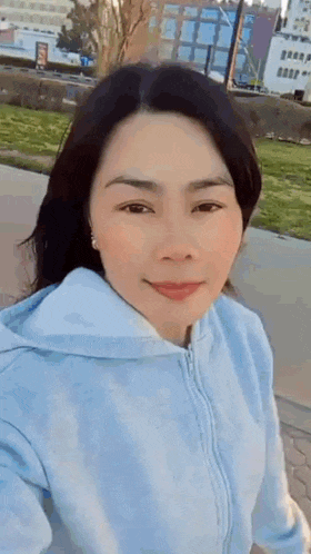 a woman is taking a selfie in a park wearing a blue hoodie .