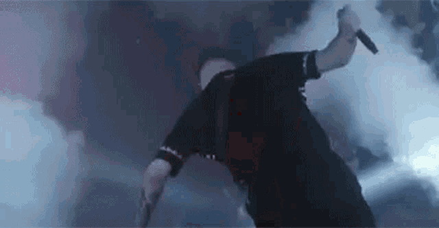 a man is standing on his back on a stage holding a microphone and smoke is coming out of his mouth .