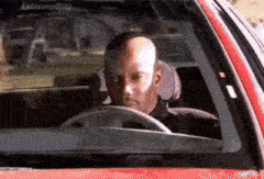 a bald man is driving a red car with the word extremeblitz on the windshield