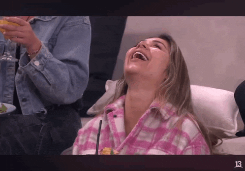 a woman in a pink plaid shirt is laughing and holding a drink in her hand