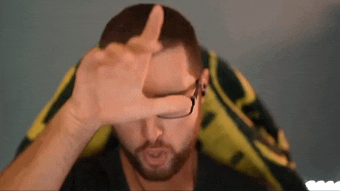 a man with a beard and glasses is covering his face with his hands .