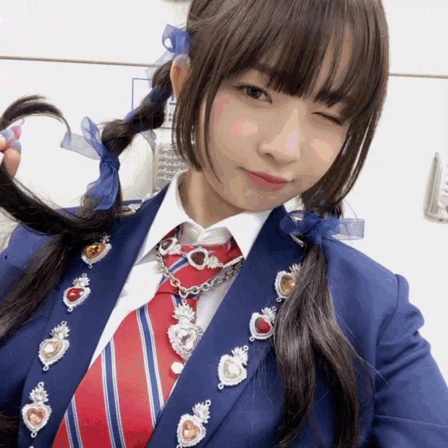 a girl wearing a blue jacket and a red tie has a necklace with hearts on it