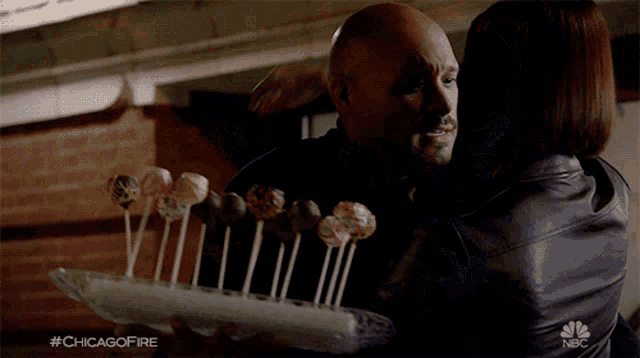 a man and woman hugging while holding a tray of marshmallows and cupcakes