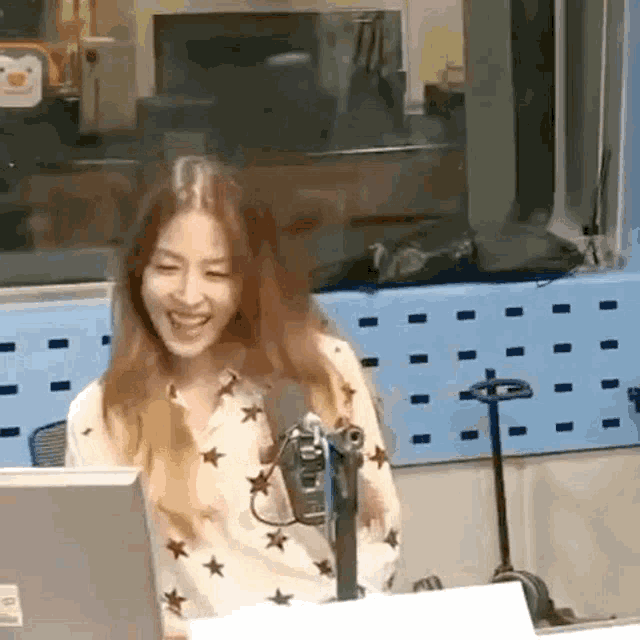 a woman is smiling while sitting in front of a microphone in a radio studio .