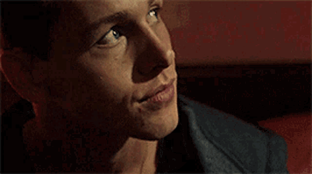 a close up of a man 's face with blue eyes and freckles sitting on a red couch .