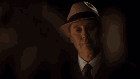 a man wearing a hat and a tie looks at the camera