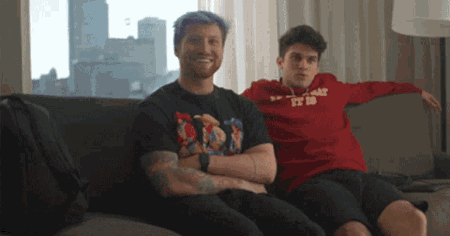 two men sitting on a couch with one wearing a red sweatshirt that says " it is "