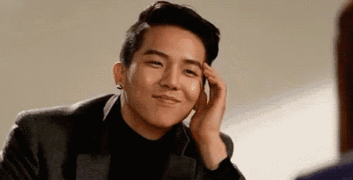 a young man in a suit and black turtleneck is smiling and touching his forehead .