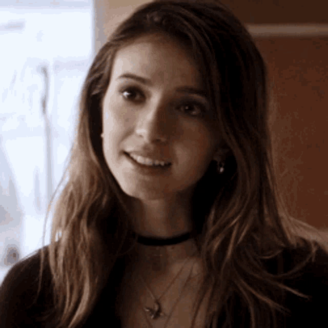 a woman with long hair is wearing a choker necklace and earrings and smiling .