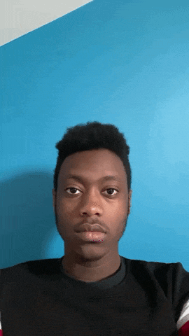 a young man in a black shirt is looking at the camera in front of a blue wall