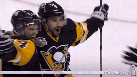 two hockey players are celebrating a goal on the ice with their arms in the air .