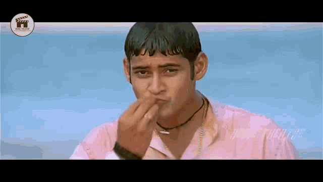 a man in a pink shirt is holding his hand to his face