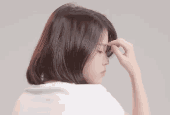 a woman in a white shirt touches her forehead