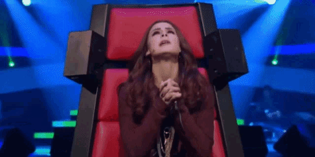 a woman is sitting in a red chair with her hands folded in front of her face
