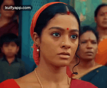 a woman with a nose ring is standing in front of a crowd of people and making a funny face .
