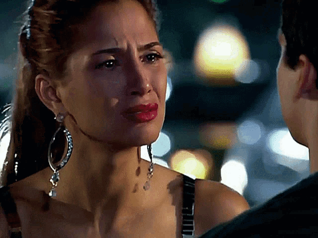 a woman wearing hoop earrings looks at a man with a sad look on her face