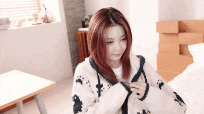 a woman with red hair is sitting on a bed wearing a white and black sweater