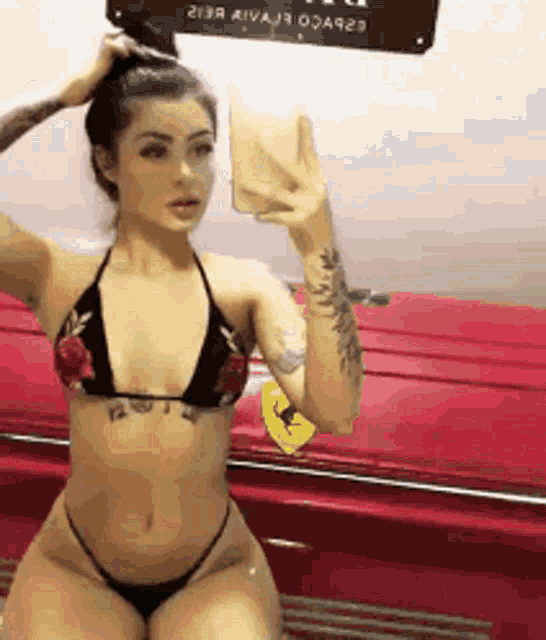 a woman in a bikini taking a selfie in front of a red car