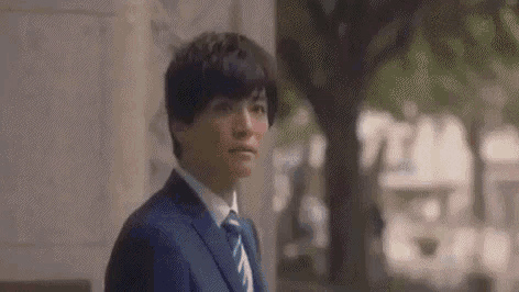 a man in a suit and tie is standing in front of a building and looking at the camera .