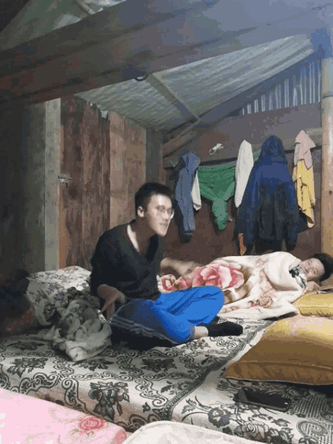 a man sits on a bed next to another man sleeping