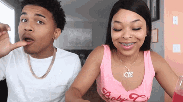 a woman wearing a pink tank top with the word baby on it is sitting next to a man