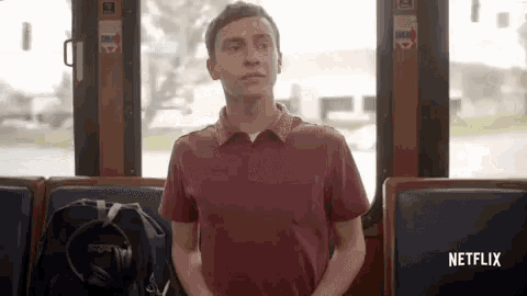a man in a red shirt is sitting on a bus with his backpack .