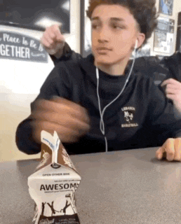 a boy is sitting at a table with a box of awesome milk