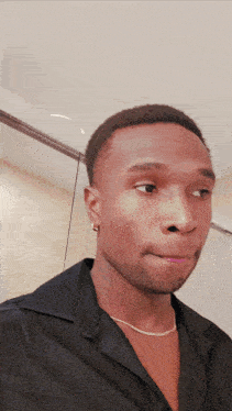 a young man wearing a black shirt and a gold chain around his neck looks at the camera