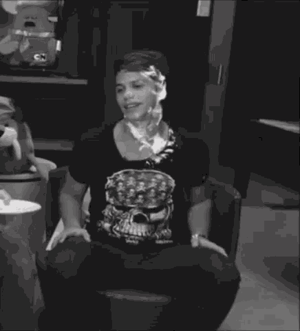 a man wearing a black shirt with a skull on it is sitting with a plate of food in front of him
