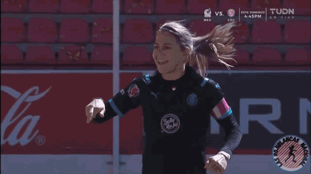 a female soccer player stands in front of a coca cola advertisement