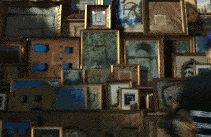 a blurred image of a man standing in front of a wall of framed pictures including one that has the letter p on it