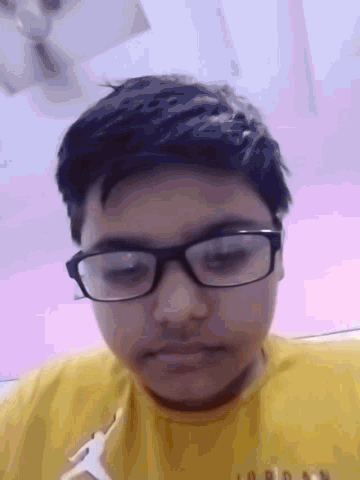 a young man wearing glasses and a yellow shirt looks down at the camera